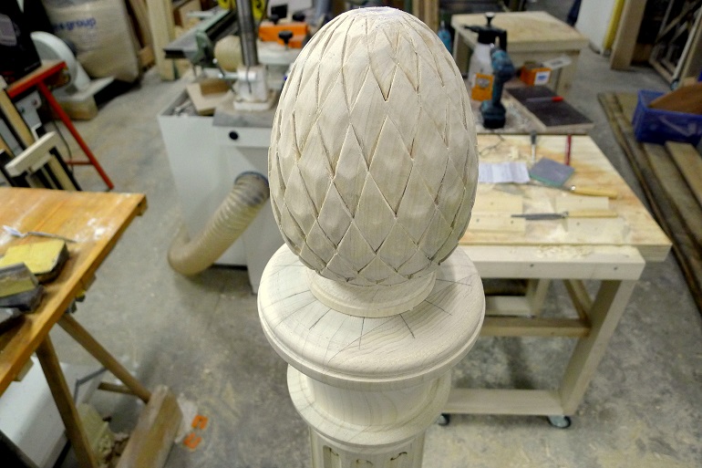 Handgesneden dennenappel als bekroning van de gecanelleerde trappaal. Handgesneden dennenappel als bekroning van de gecanelleerde trappaal.